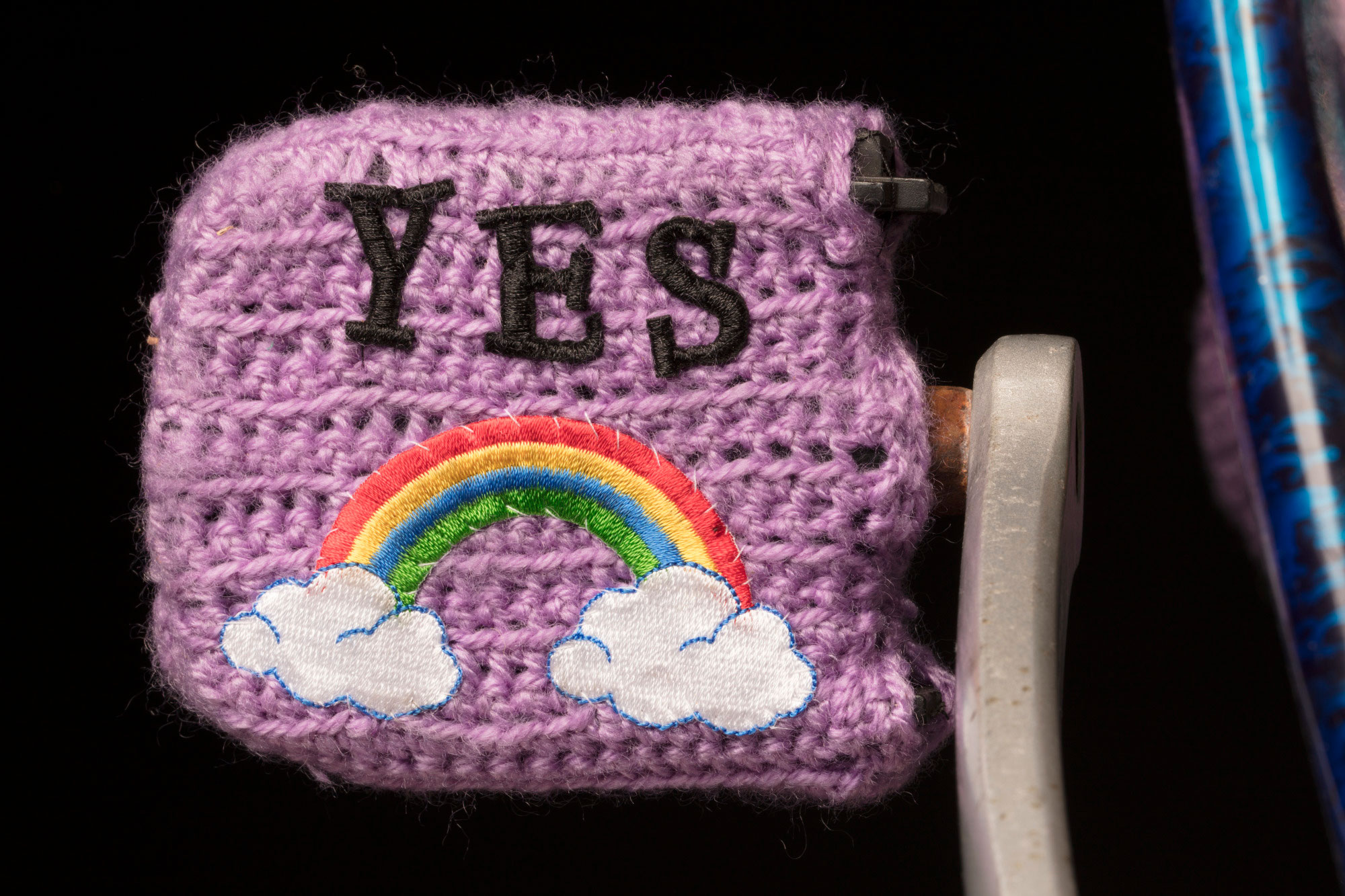 <p>Bike pedal covered in woollen crochet and the word ‘yes’ embroidered on it</p>
