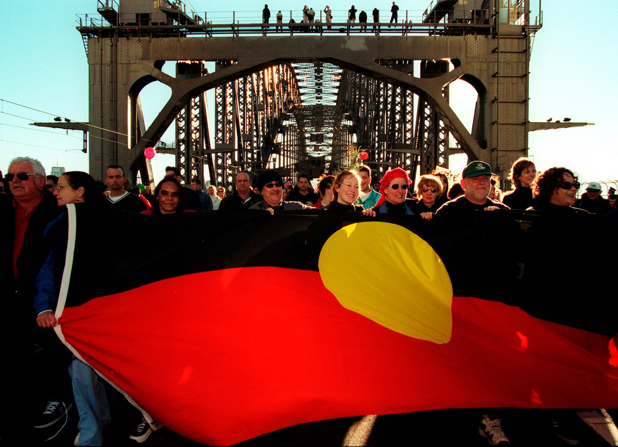 Participants in the 2000 Walk for Reconciliation hold up the Aboriginal flag.