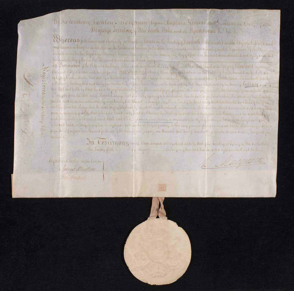 A handwritten white coloured vellum land grant made out to Gregory Blaxland that reads 'By His Exellency Lachlan Macquarie ...'. The document is dated 25th August 1812. The round shaped seal hangs freely from the bottom, attached by a beige coloured ribbon.