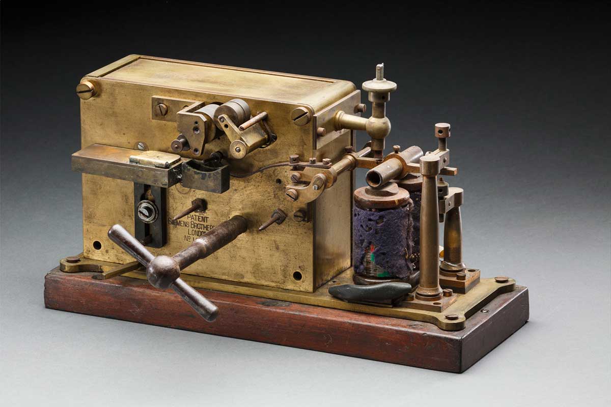 A Siemens Brothers Morse Code printing machine with a brass body mounted on a timber base. The printer is branded "Silvertown".