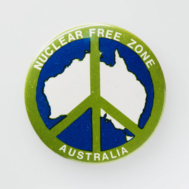 Badge featuring Australia overlaid with a peace symbol. Around the edges is printed with the text 'Nuclear Free Zone / Australia’.