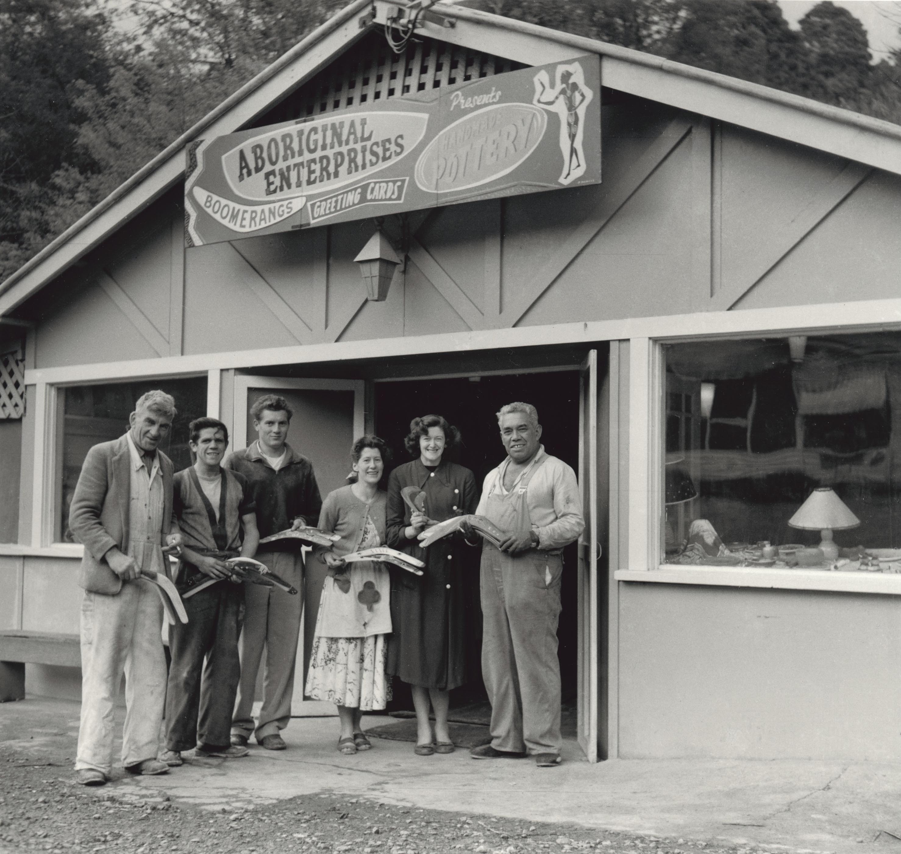 Six people standing outside a shop holding boomerangs