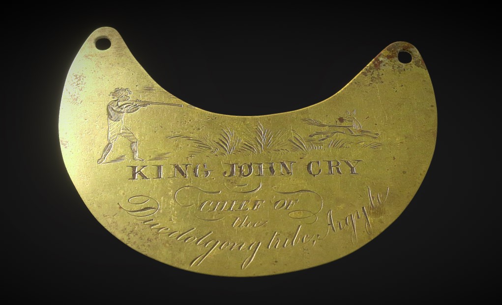 A crescentric brass breastplate with a hole at the edge of each horn to attach a chain. "KING JOHN CRY / CHIEF OF / the / Duedolgong Tribe, Argyle" is engraved on the anterior surface. A man with a rifle is engraved on the left horn, and a fox is engraved on the right horn.