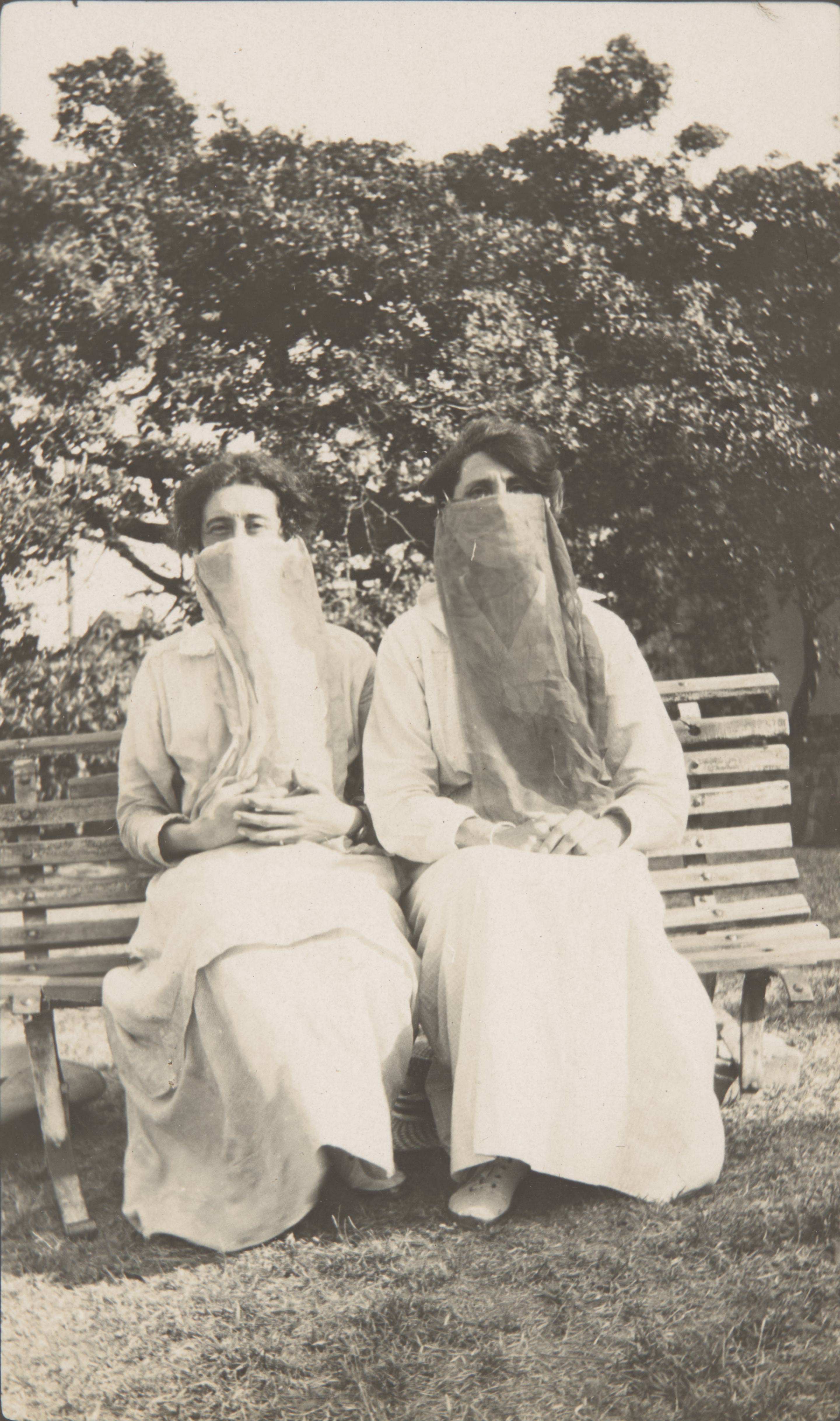 Two women wearing face scarves sitting on a park bench during the Spanish flu pandemic, 1918
