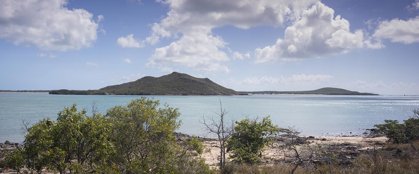 Photograph of an island with coastline in the foreground. 