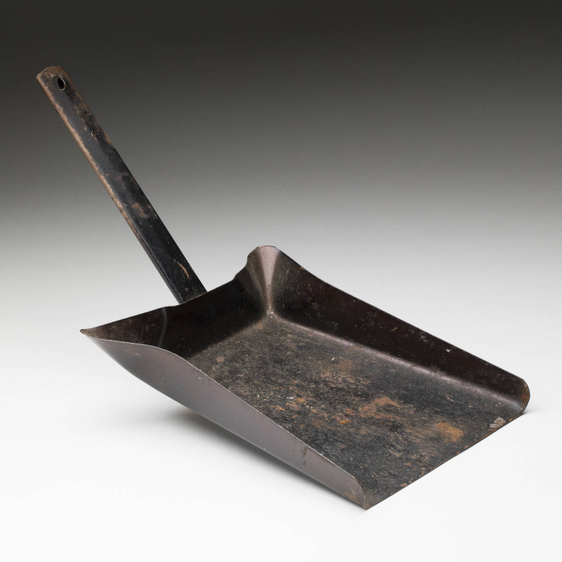 A dustpan made of metal and painted black. Three sides of the dust pan are curved up.