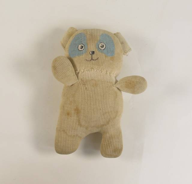 A discoloured and stained cream cotton rib sock toy that has a painted face depicting a dog with blue patches around the eyes.