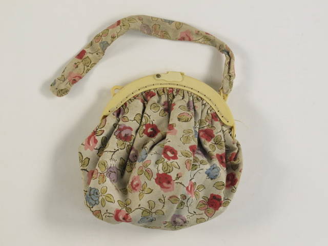 A homemade white with floral design bag and strap with a plastic frame and clasp.