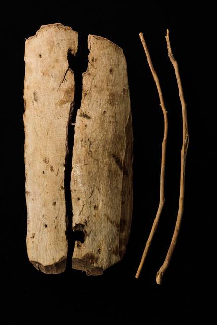 A wooden oval-shaped toy shield with a handle made from two sticks which are inserted through holes on the posterior surface.