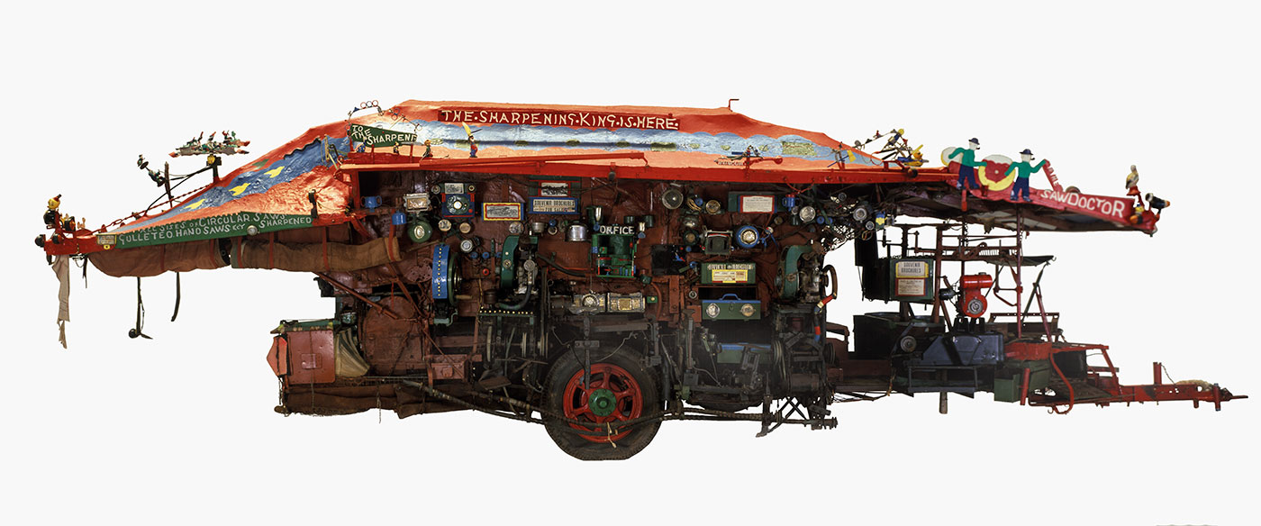 Side view of an elaborately decorated wagon on a single axle, with a red canvas roof and various tools, compartments and handmade signs.