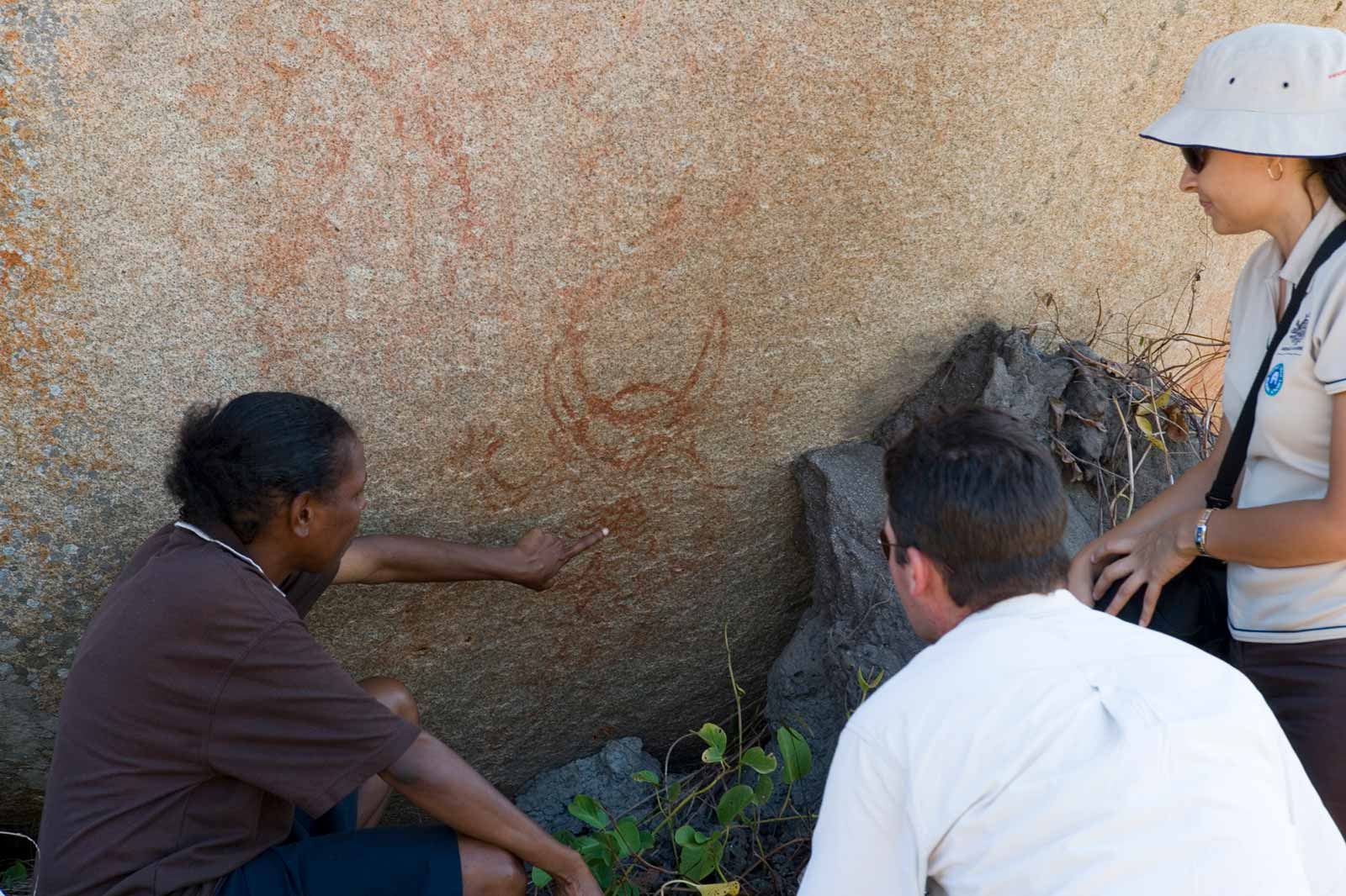One person points to an example of rock art, while two others look on.