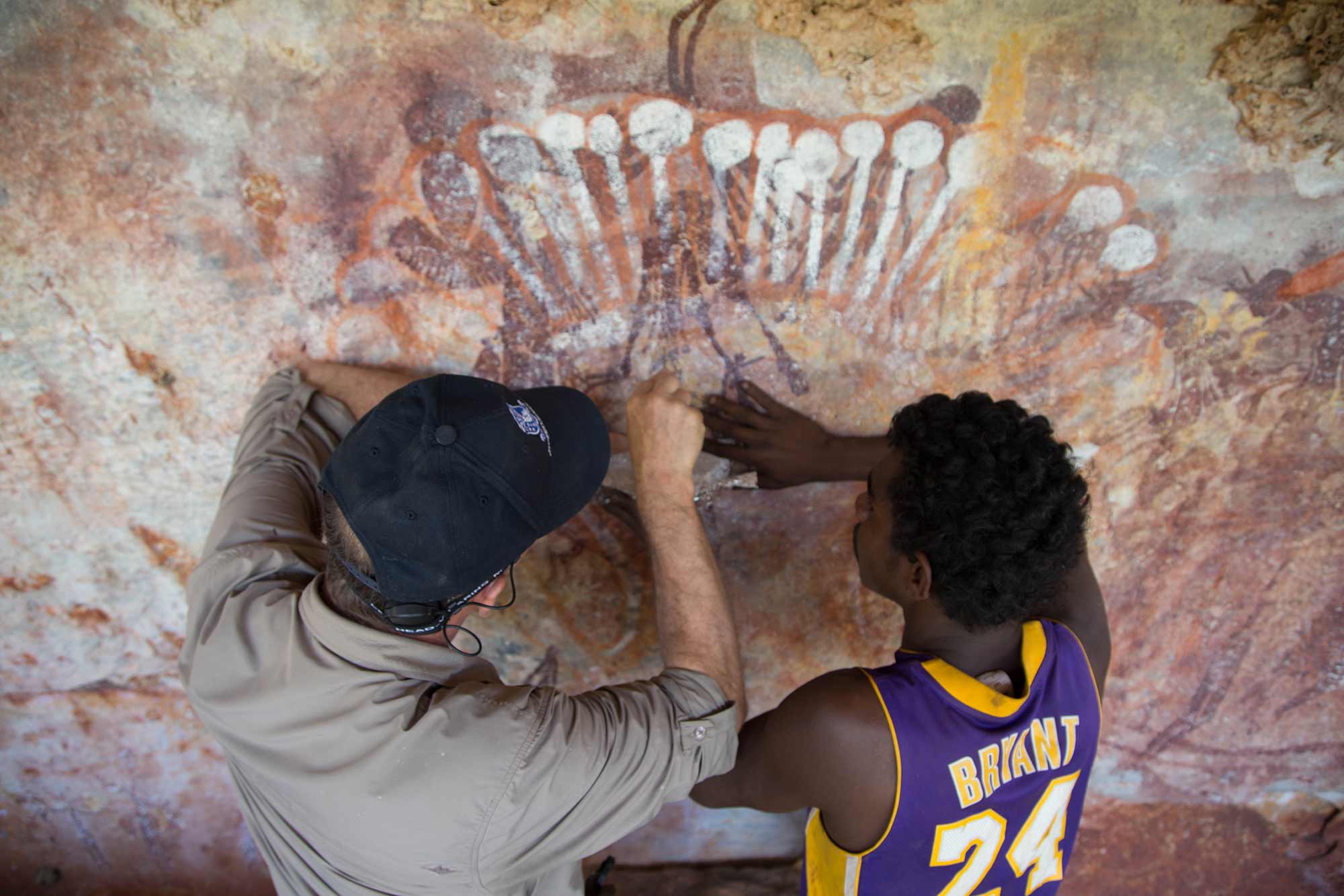 Photograph of two men scraping a sample of paint from rock art.