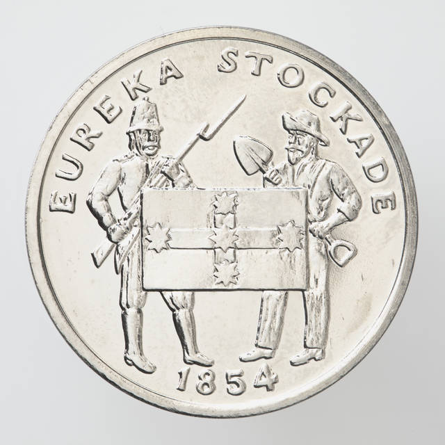 A silver coloured metal commemorative medal depicting the Eureka Stockade. A miner and a soldier flanking a Eureka Flag are depicted on the front of the medal. Text stating "Eureka Stockade" is inscribed on the top of the medal with the date "1854" is inscribed below the image. The back contains text stating "Australia 200 years - A Bicentennial medal collection" inscribed over a map of Australia with banksias and wattle plants surrounding the map.