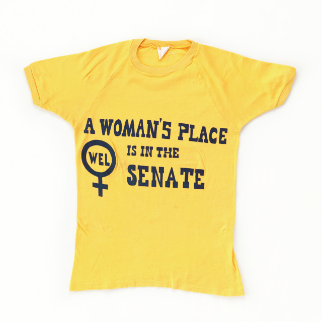 T-shirt, yellow, with 'A Woman's Place is in the Senate' printed in blue on the front of shirt.
