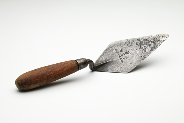 W.H.S. brand trowel of solid cast steel with a wooden handle and the text "W.H.S." engraved on the blade. The diamond shaped blade is well worn and deeply pitted.
