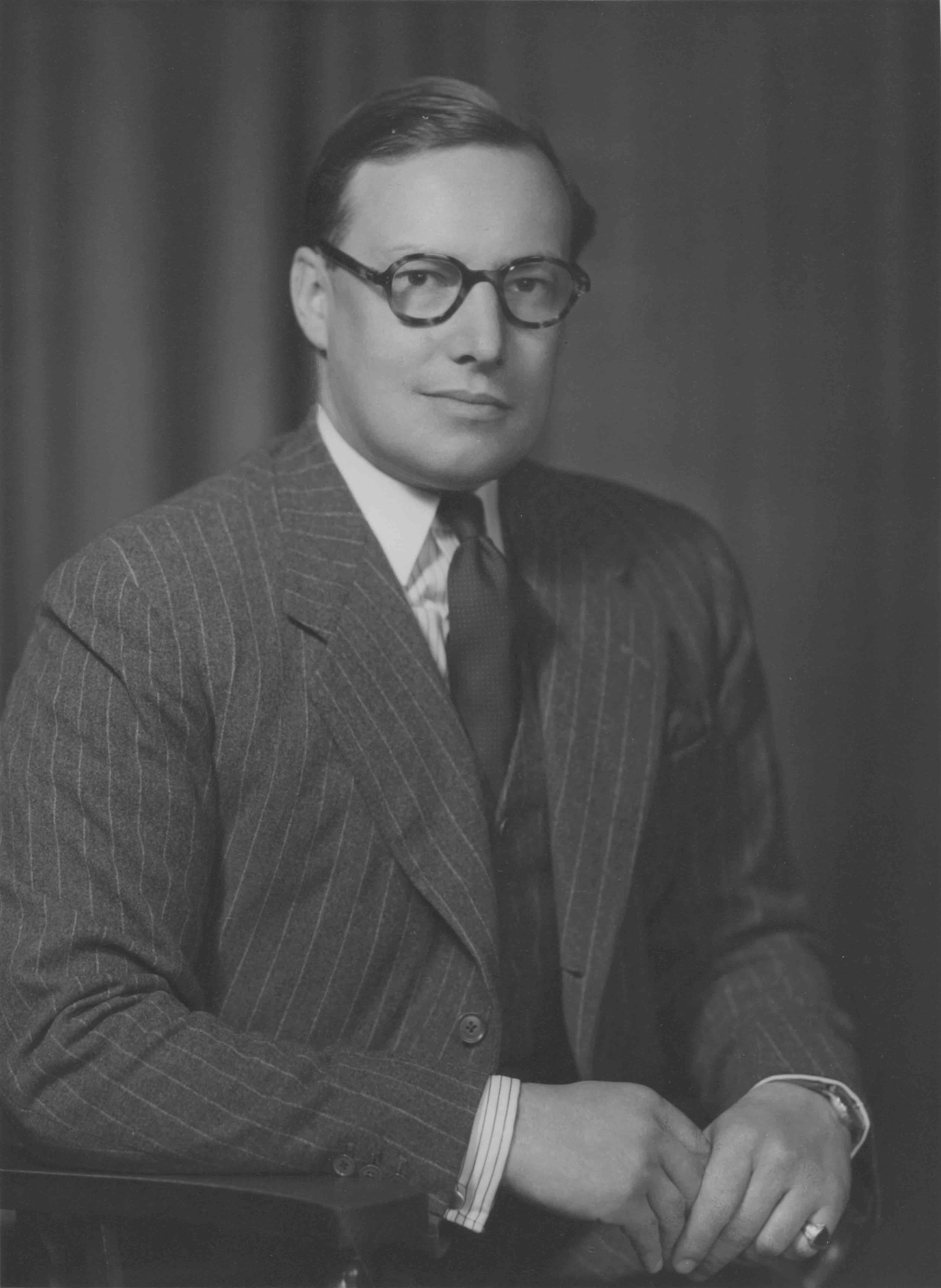 Portrait of Commander Terry Poulden wearing a pinstripe suit and glasses.
