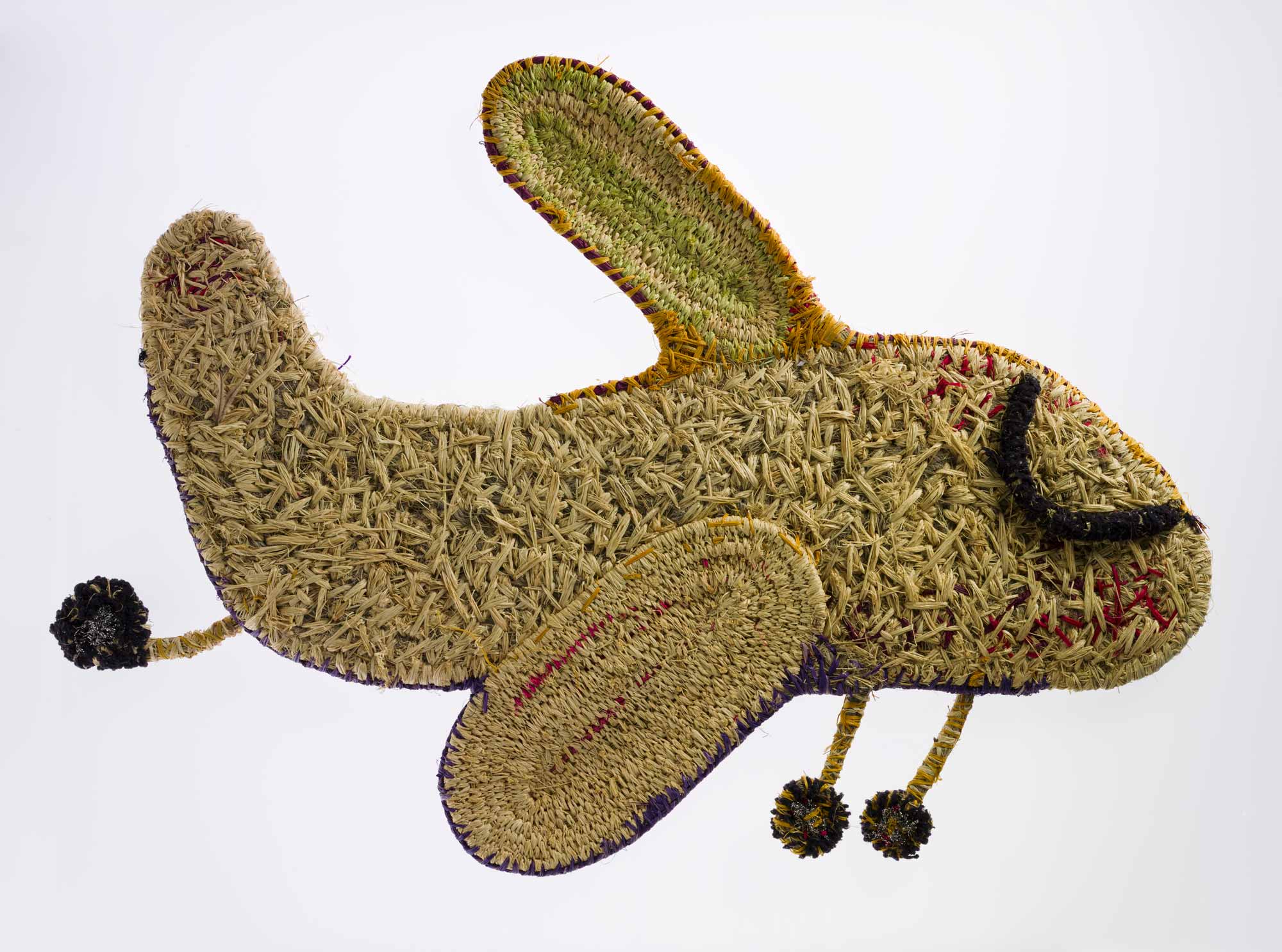 A sculpture depicting an aeroplane with its wheels down. The sculpture is made of woven grass, plant material dyed in different colours, wool and metallic thread. 