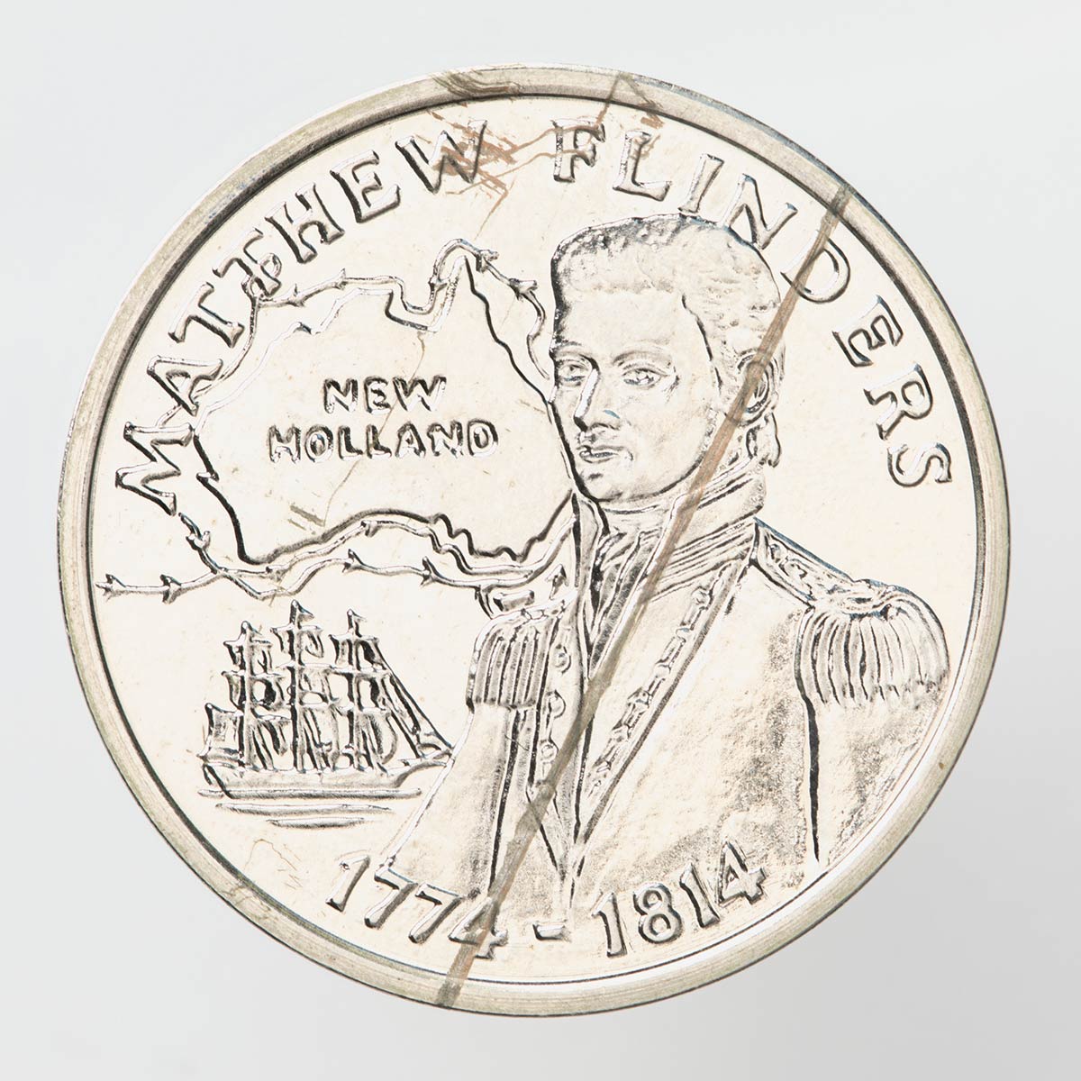 A silver coloured metal commemorative medal depicting Matthew Flinders. A map of Australia showing the routes of Flinders' voyage and an image of his Ship are also depicted. The dates "1774-1814" are inscribed beneath of image on the front.