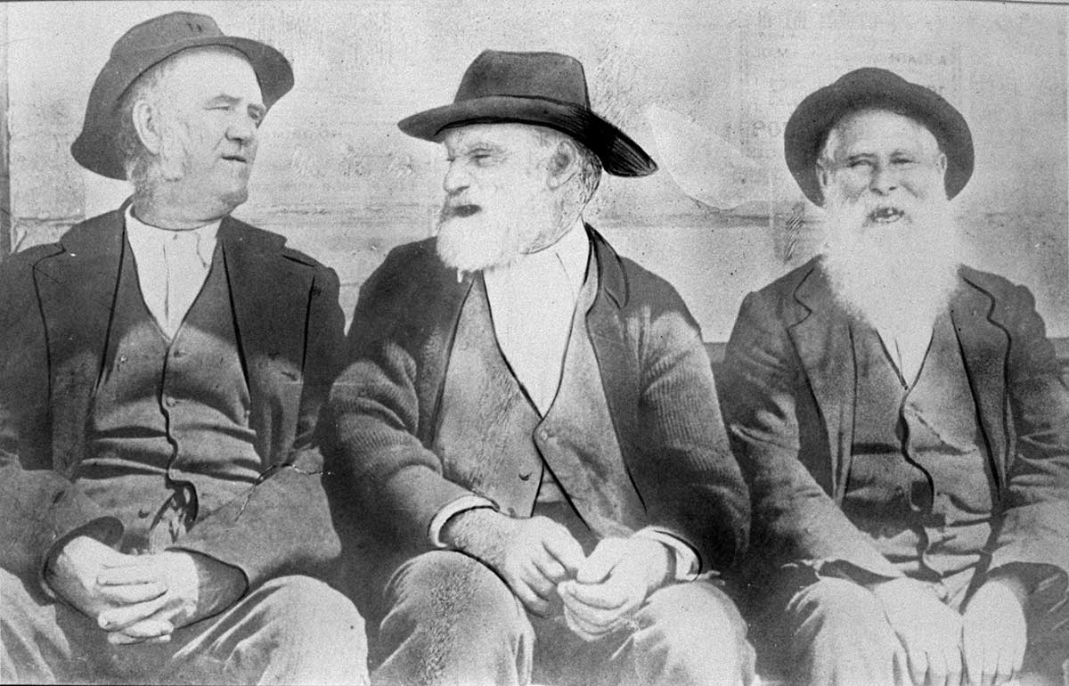 Black and white photograph of three elderly men in civilian clothing sitting in a row.