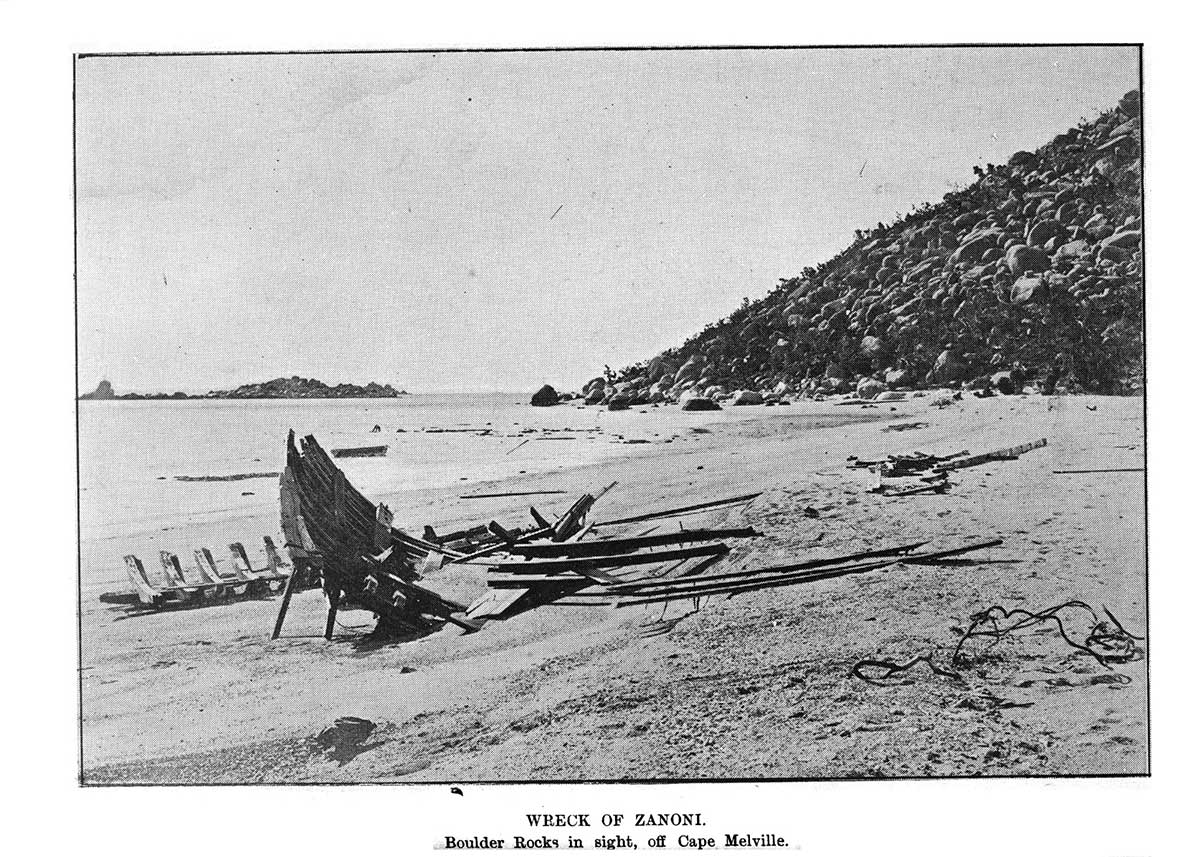 Black and white photograph of a wreck of a small ship on a deserted beach.