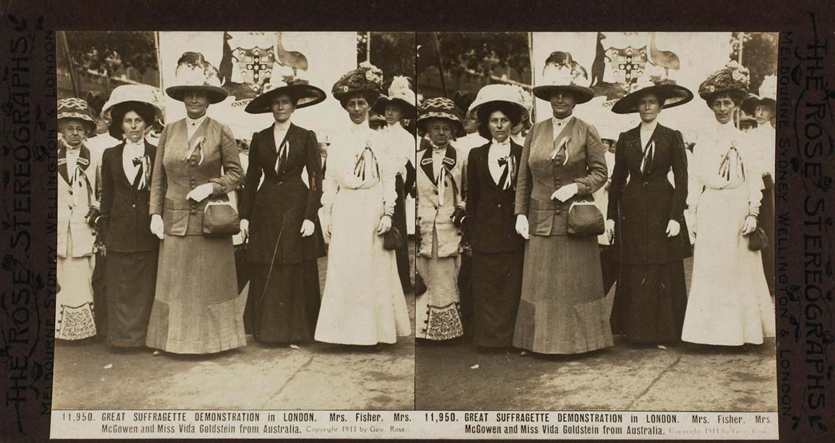 Black and white photograph showing a group of women standing formally in front of a partially visible banner bearing the Australian coat of arms.