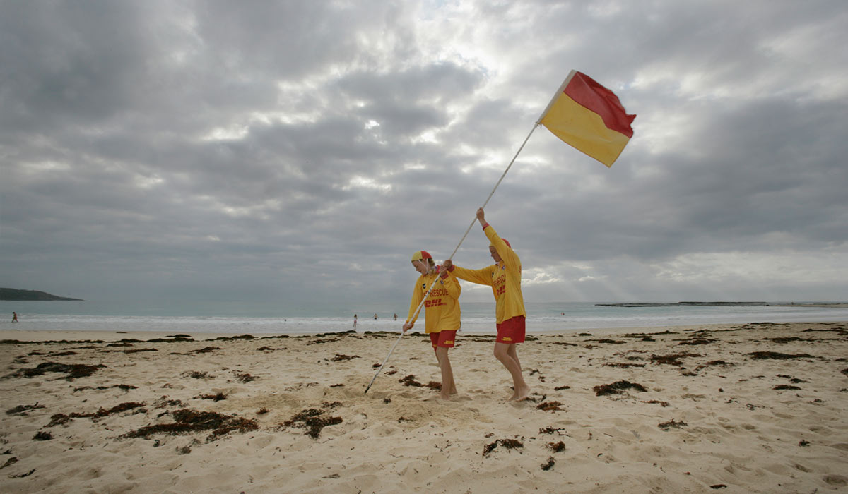 Two young people plant a lifesaving flag in almost deserted beach.