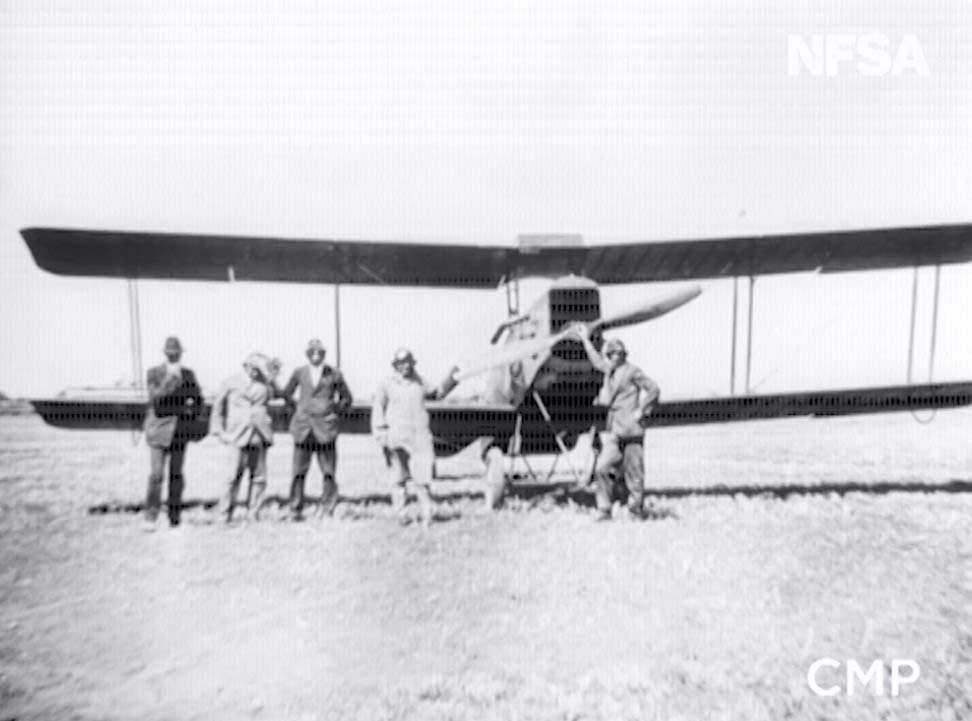 Film still featuring a group of men in front of an aeroplane.