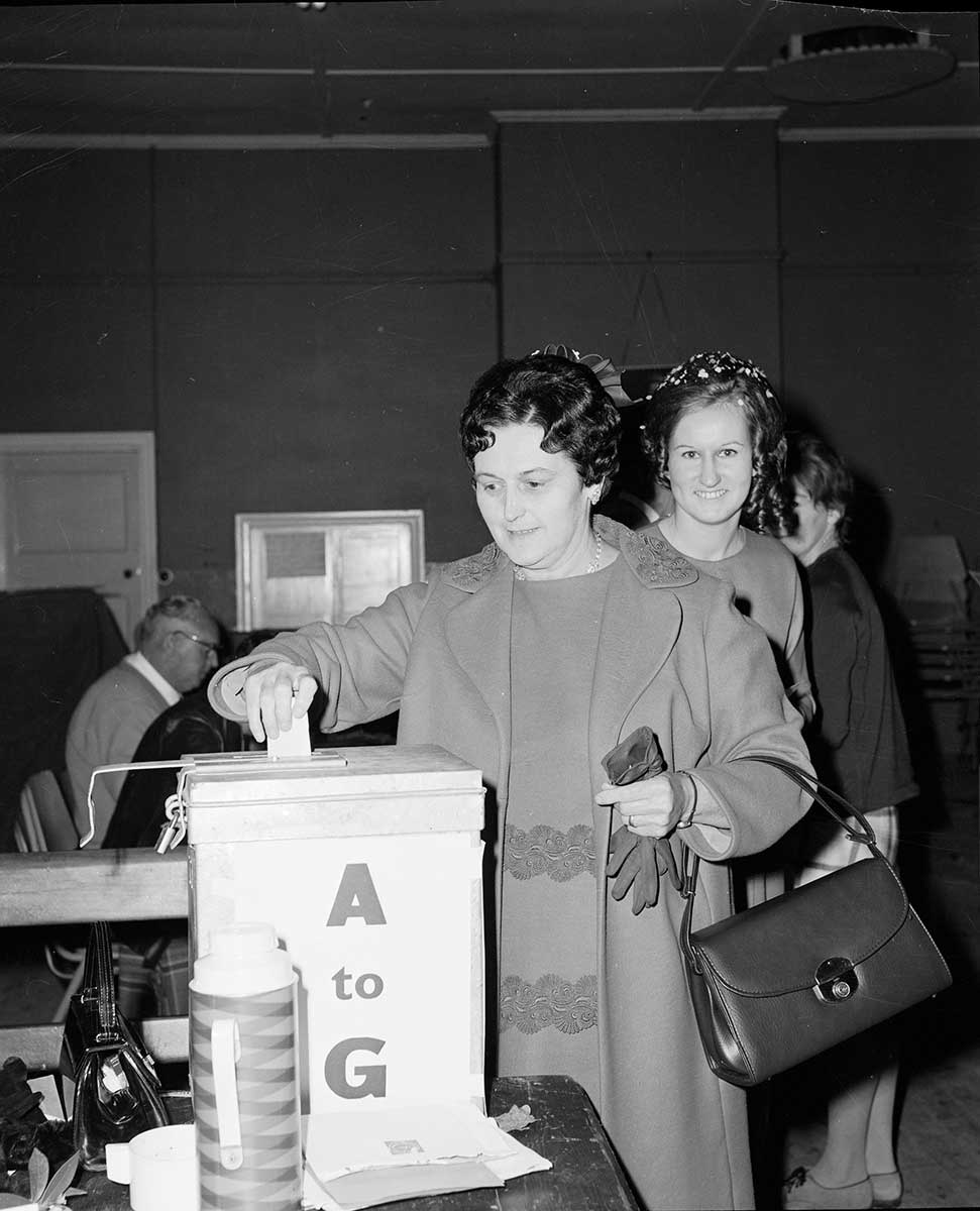Black and white photograph of women posting their votes at a polling booth.
