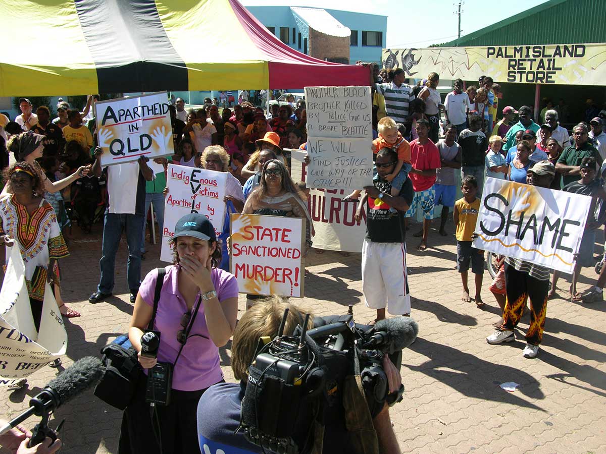 An organised protest of people gathered in front of the media. They are holding hand-written placards with various anti-racial slogans.