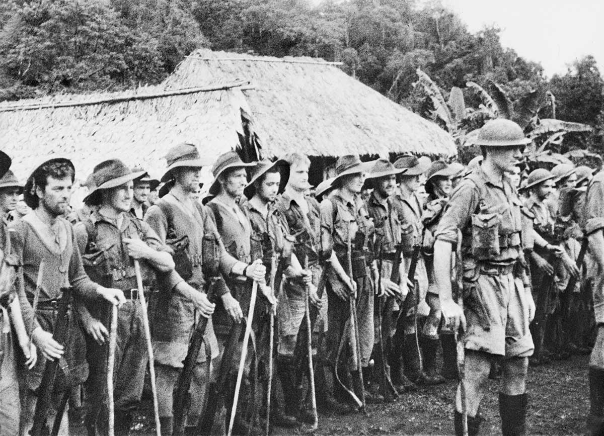 Black and white photograph of Australian soldiers standing in rows in front of a thatched hut.