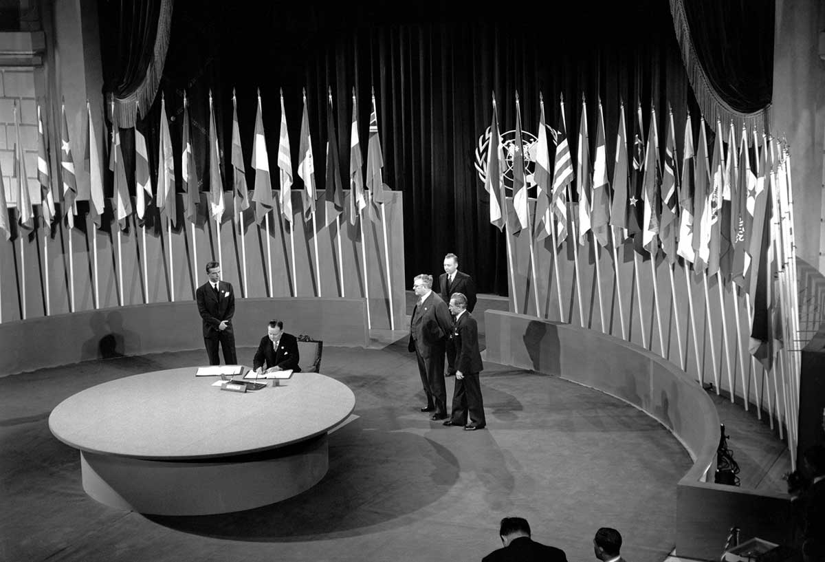 Black and white photograph of Francis Michael Forde signing the UN Charter at a ceremony held at the Veterans' War Memorial Building.