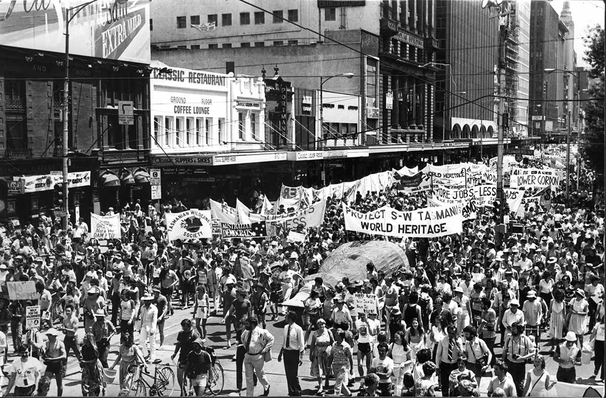 Black and white photograph of crowds of peaceful protestors walking through a city street. They are holding banners supporting the Franklin River campaign.
