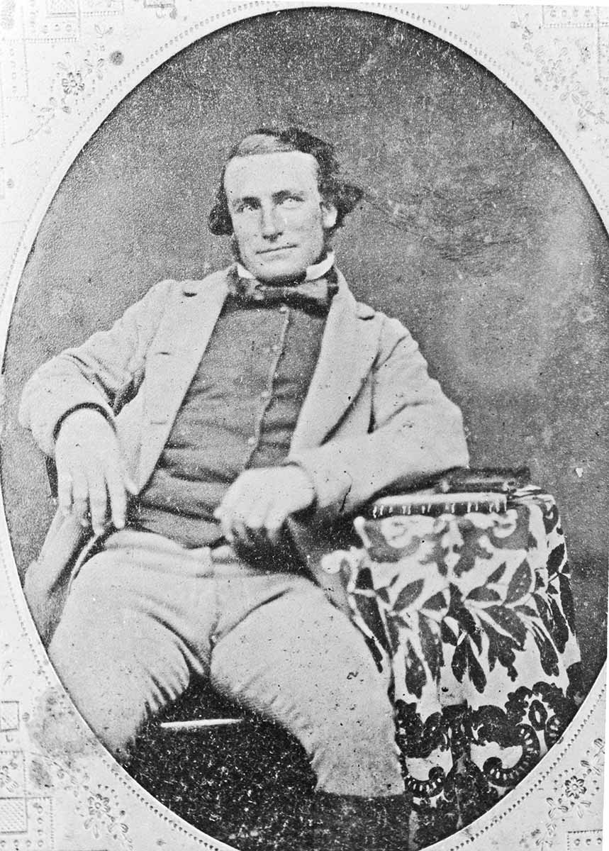 Black and white portrait photograph of a man sitting back casually with a mused expression.