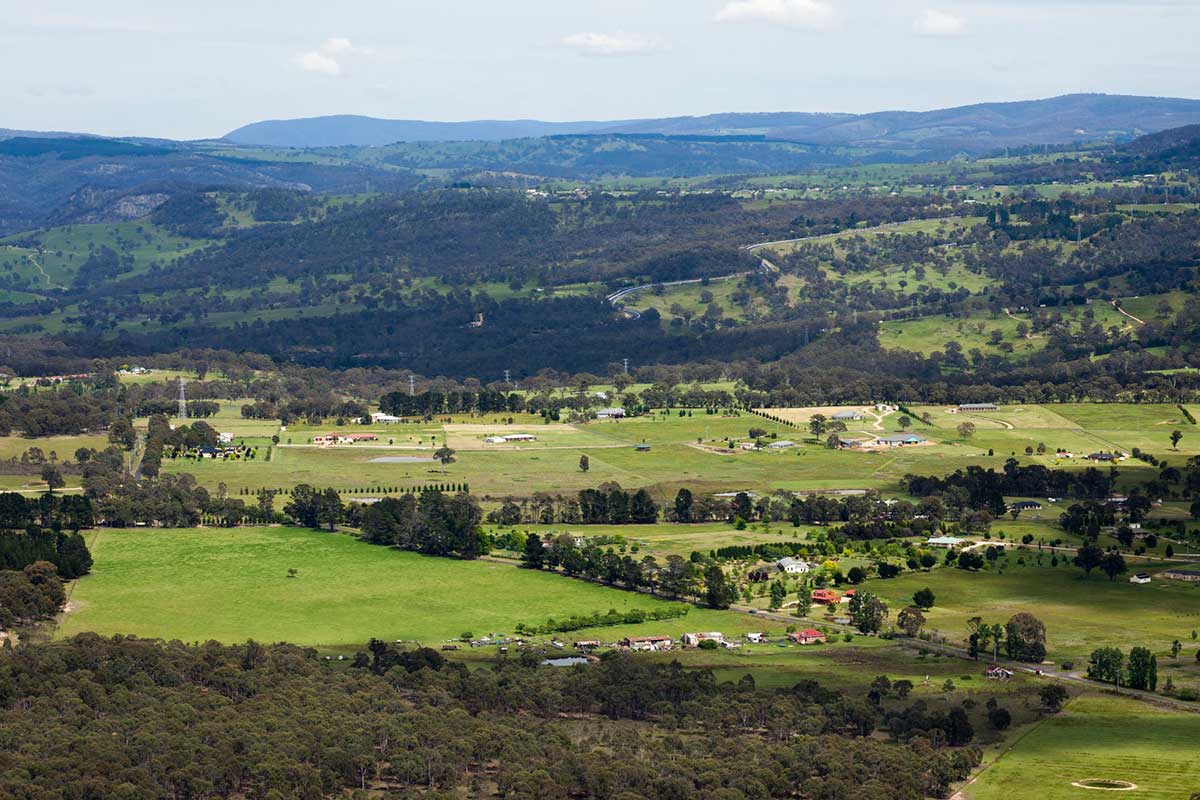 Colour photograph of a lush landscape featuring a town with mountain ranges beyond.