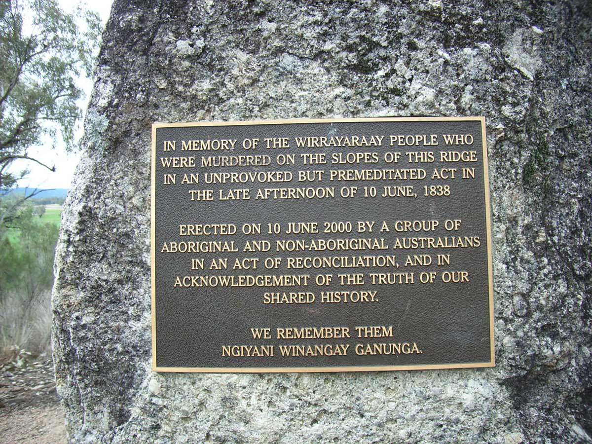 A memorial plaque fixed to a rock surrounded by bushland. The plaque is in memory of the Wirrayaraay people and erected on 10 June 2000.