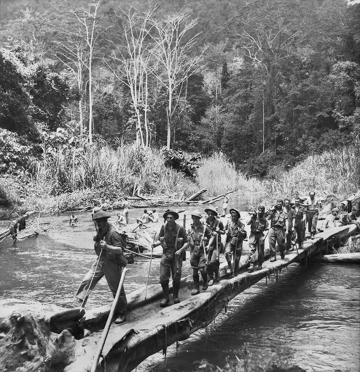 About 20 soldiers use a simple bridge that is little more than a pair of logs.