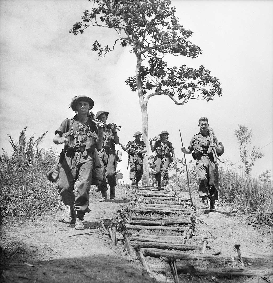 Black and white photograph of a group of Australian soldiers walking down a hill with a makeshift staircase in the centre of the group.