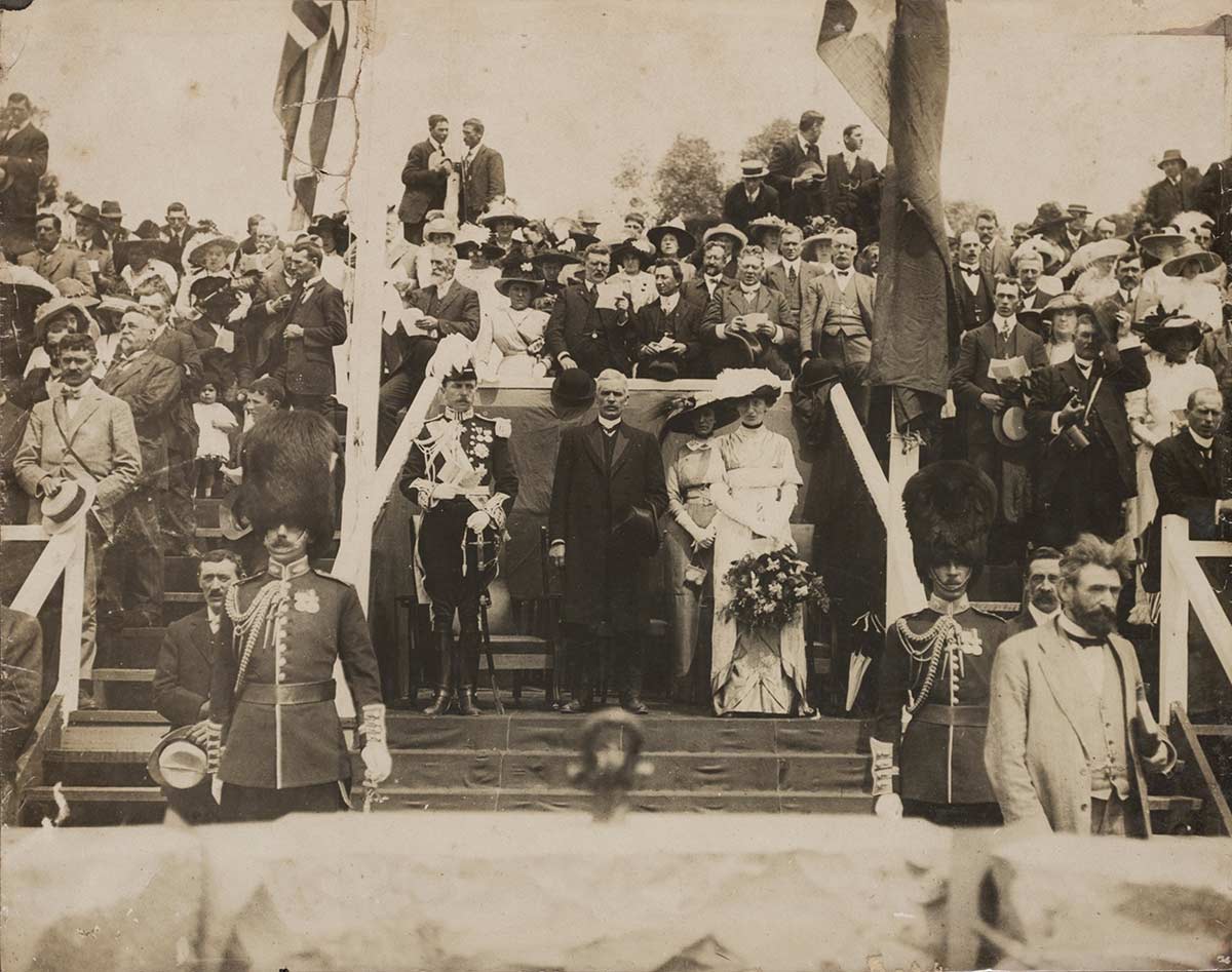 Black and white photograph of an official ceremony overseen by officials, soldiers in regalia, and a large crowd of spectators.