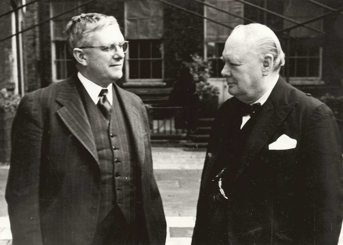Evatt and Churchill stand next to each other looking at each other.