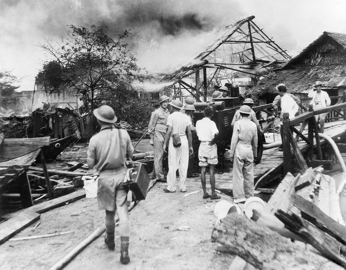 Black and white photograph of Australian soldiers and villagers surveying the aftermath of military attacks.