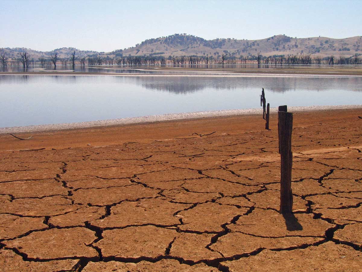 Colour photograph of a lake with low water levels and dried cracked soil around the edges.