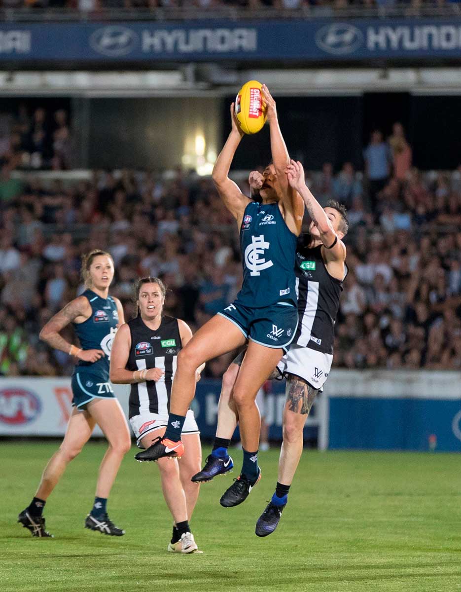 Four women on the field line up to catch a football during an AFL game.