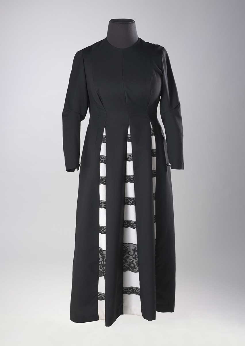 A black long-sleeved dress with a scoop neck, and three white panels extending from the waistline with black lace overlay.