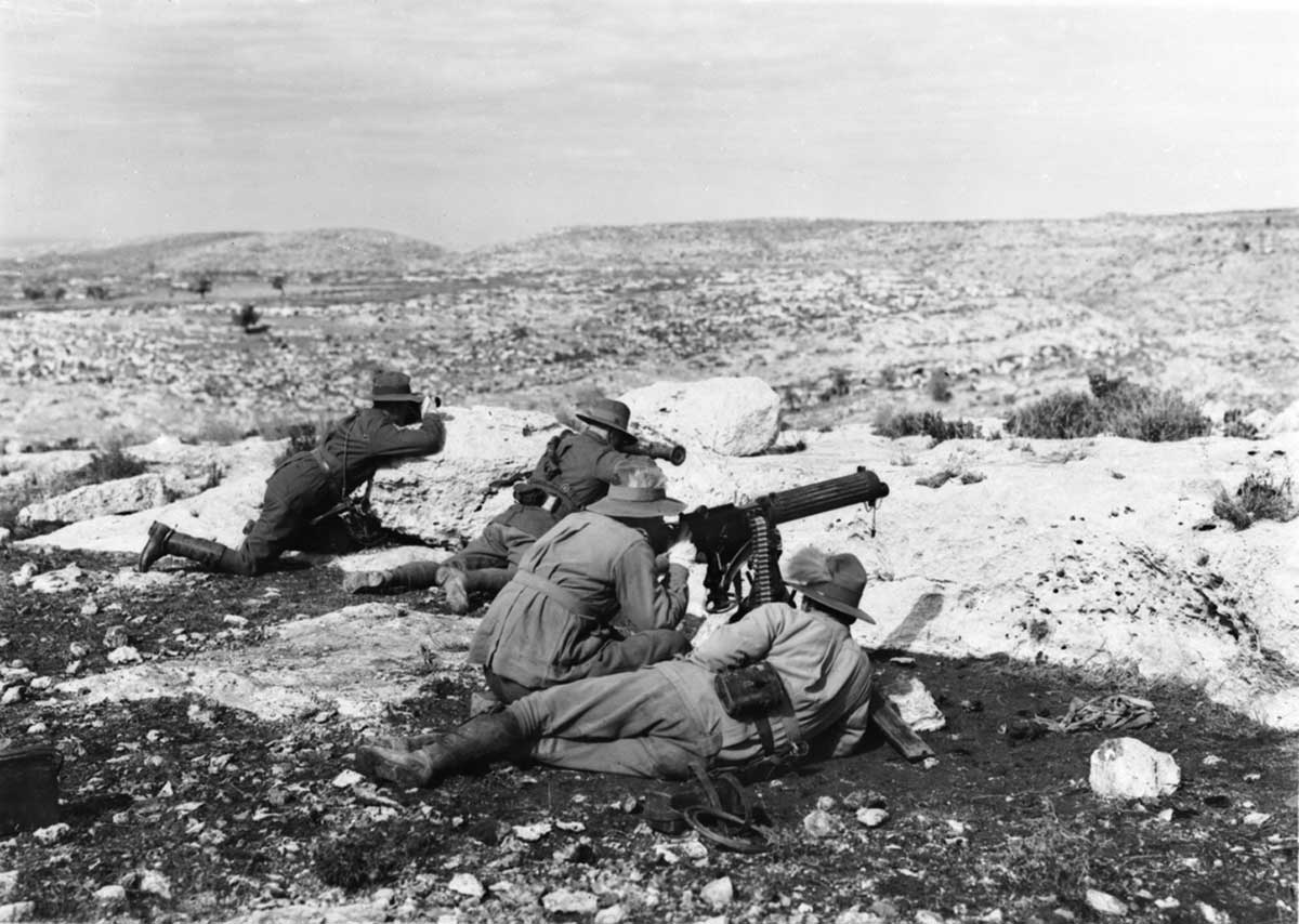 Black and white photograph of four Australian soldiers overlooking barren terrain while lying low with weapons.