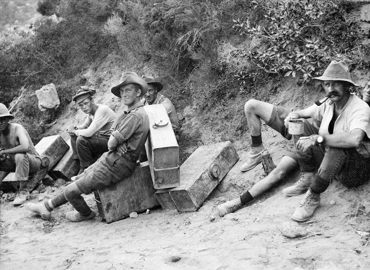Black and white photo of a handful of Australian soldiers resting on or near their suitcase-sized water containers.