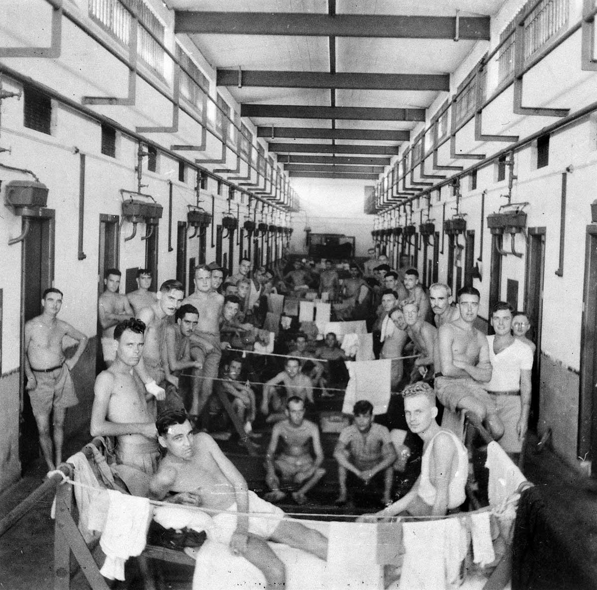 Black and white photograph of half-dressed men gathered in the hallway of a prison.