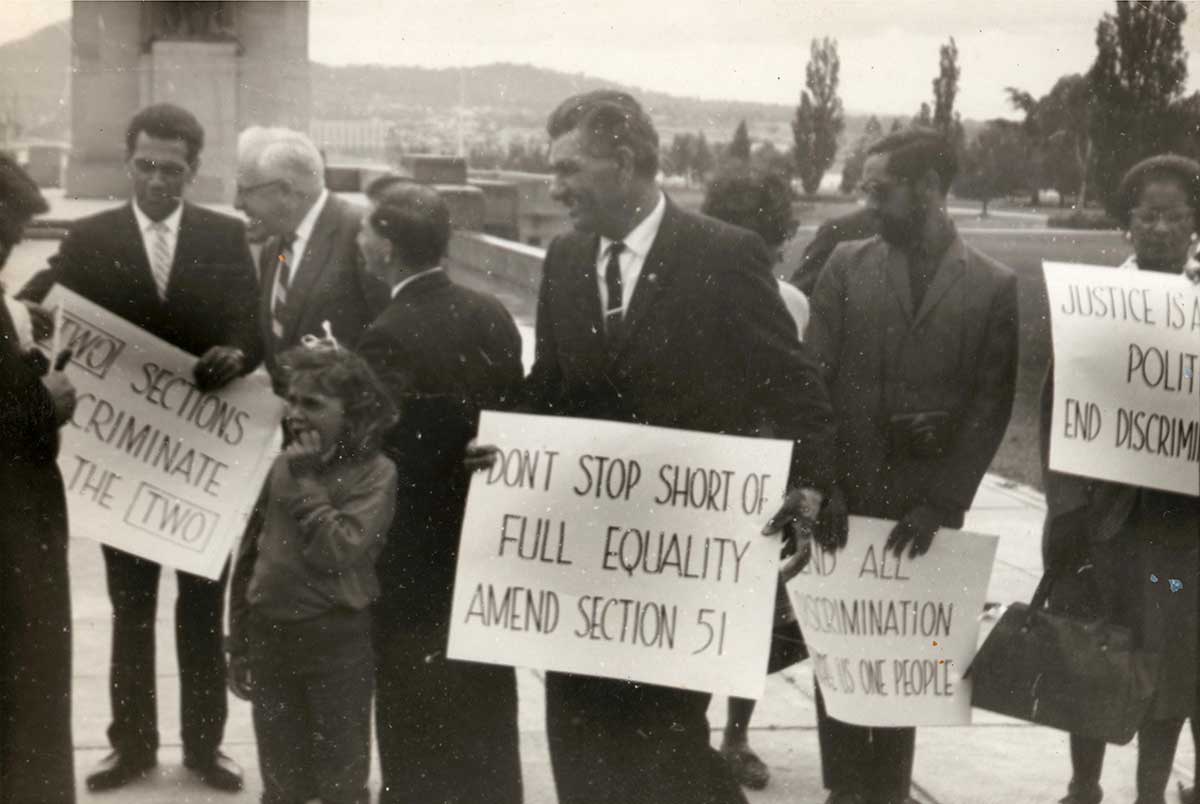 Black and white photograph of protestors in support of the 1967 Referendum holding placards outside Parliament House in Canberra, Australia.