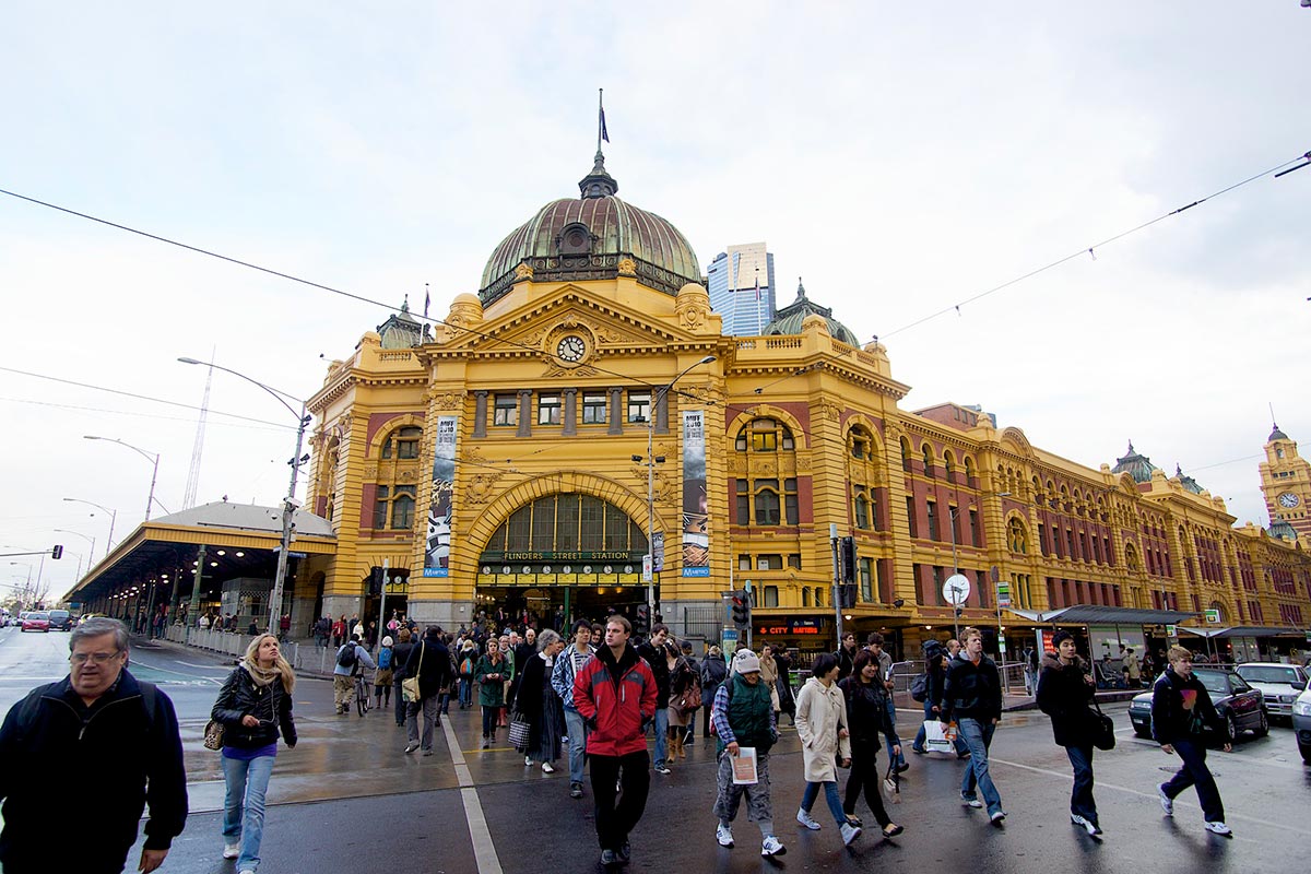 Pedestrians entering and exiting a Federation style building. A sign above the entrance reads 'FLINDERS STREET STATION'.