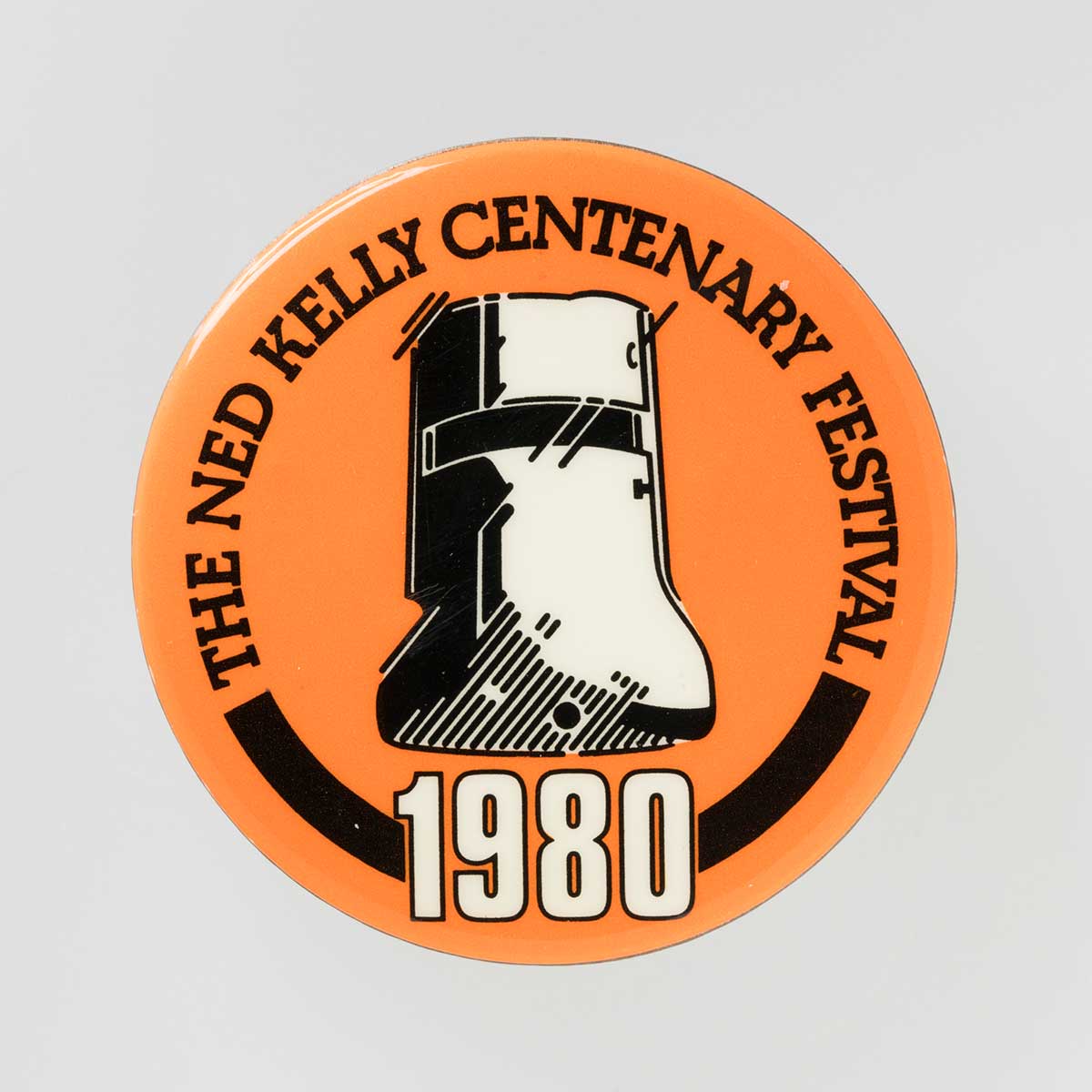 Circular badge. Black and white sketch depicting Ned Kelly mask on orange background. Black text around edge of badge "Ned Kelly Centenary Festival'. White text below mask "1980'.