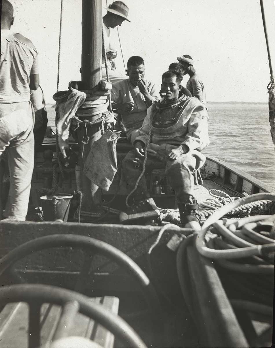 Black and white photograph of a small group of men sitting and standing on the deck of a sailing vessel.